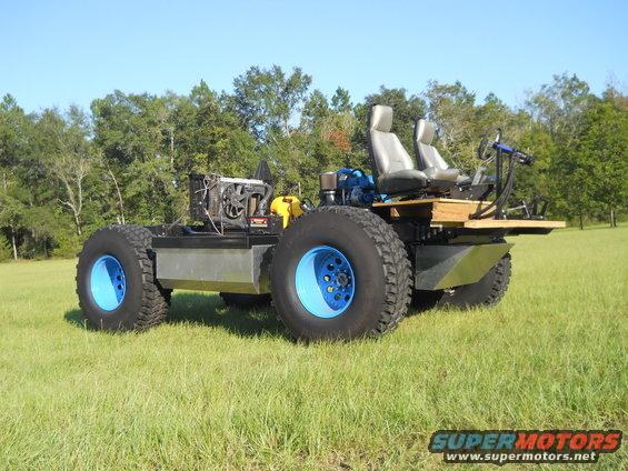 Amphibious all-terrain vehicle with large blue-rimmed tires, dual seats, and exposed engine components, parked on a grassy field