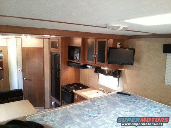 RV interior with kitchen, refrigerator, microwave, stovetop, sink, and bed