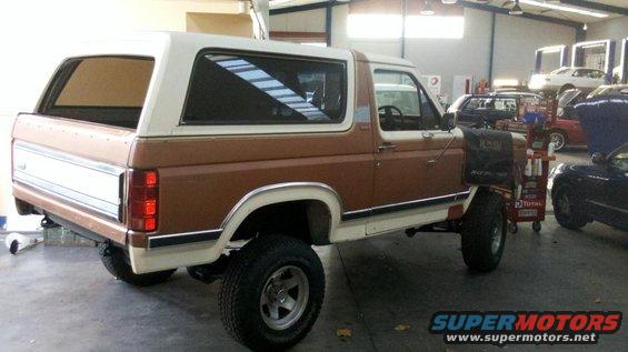 Brown and white Ford Bronco parked in a garage with other cars