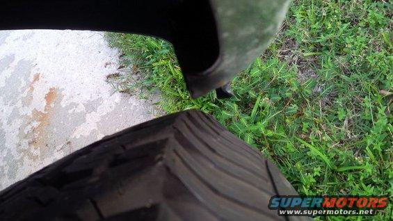 Close-up of a tire tread and a vehicle fender over grass and concrete