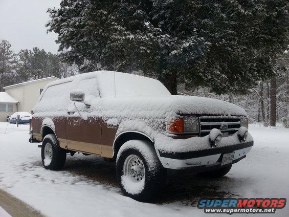 1991 Ford Bronco covered in snow, parked in a driveway