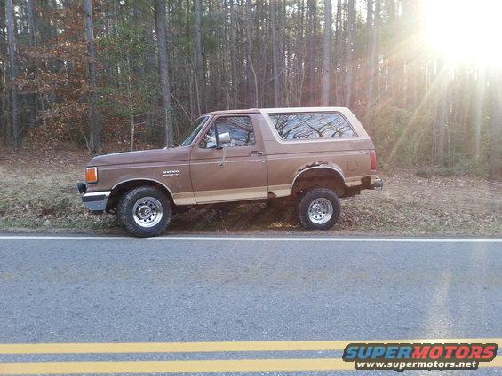 Brown Ford Bronco parked on the side of a road with trees in the background