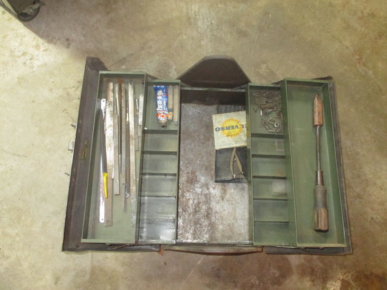 Open metal toolbox with assorted tools including files, a tube of lubricant, screws, and a screwdriver