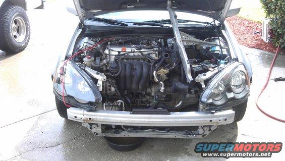 Car engine bay with front bumper removed, showing engine components and wiring