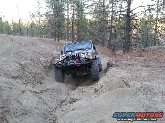 Silver Jeep Wrangler driving down a dirt trail, front bumper with winch, auxiliary lights
