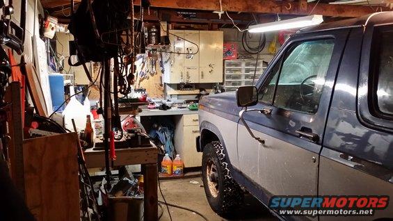 Side view of a blue and grey Ford Bronco parked in a garage with tools and supplies visible