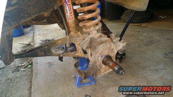 rusted front suspension assembly with a shock absorber and coil spring, supported by jack stands