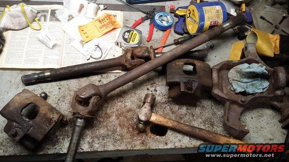 Rusty driveshaft, U-joints, and suspension components laid out on a workbench with tools