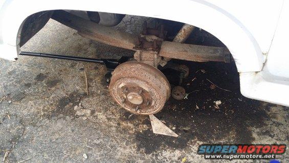 White vehicle's rusty rear drum brake and leaf spring suspension, jacked up