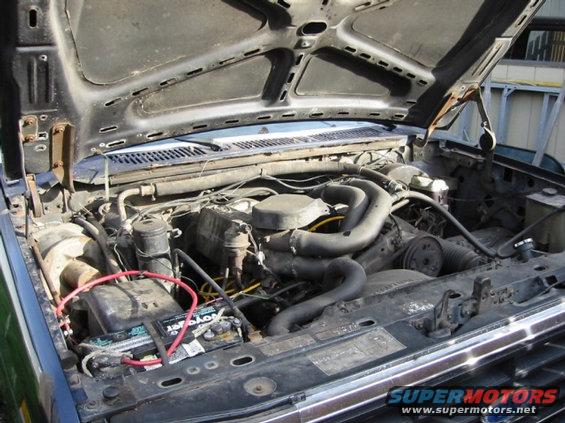 1985 Ford Bronco engine bay with V8 engine, battery, and hoses visible