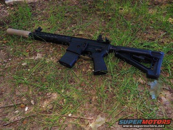 Assault rifle with suppressor and adjustable stock lying on grass