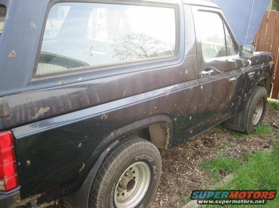 Dark blue Ford Bronco, side view, hood up, parked on dirt and grass