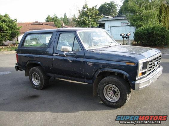 Dark blue Ford Bronco parked on a street in front of houses. It has a chrome grille and bumper