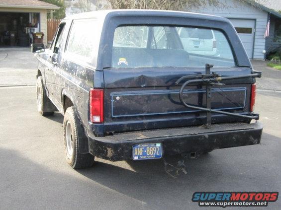 Dark blue SUV, rear view, with a bike rack and license plate ANF-8892. Dented tailgate