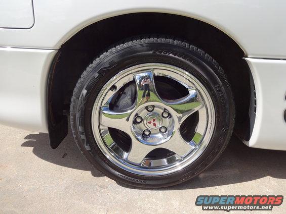 Close-up of a chrome five-spoke wheel with a Mitsubishi logo on a white car