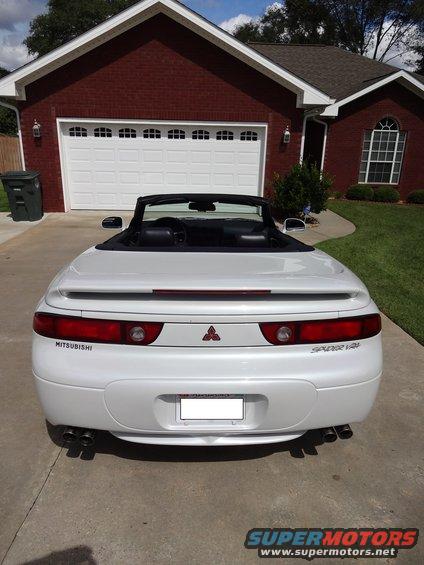 White convertible sports car parked in driveway, rear view. Features 'Mitsubishi' and 'Spider V6' badging