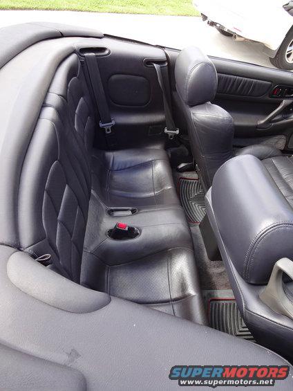 Rear leather seats and interior of a convertible. Another vehicle is partially visible outside