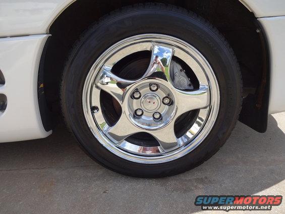 White car's chrome five-spoke wheel with a black tire and a visible 'MITSUBISHI' brake caliper