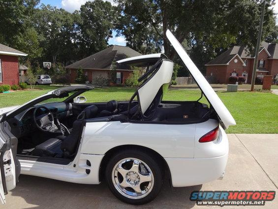 White convertible with top partially open, showing interior and rear quarter panel. Looks like a 1995 Mitsubishi 3000GT
