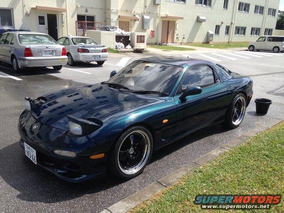 Dark green 1993 Mazda RX-7 parked next to other cars, with a black bucket nearby