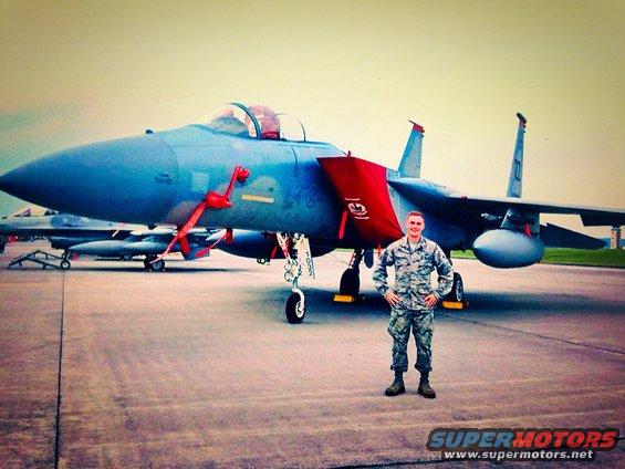 Blue fighter jet with red covers on the tarmac, an airman stands in front of it