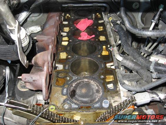 Engine block with exposed cylinders, exhaust manifolds, and timing chain. Red rags stuffed in cylinders