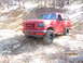 1995 Ford Bronco - Red 1995 Ford Bronco navigating a dirt path in a wooded area; white SUV visible in background.