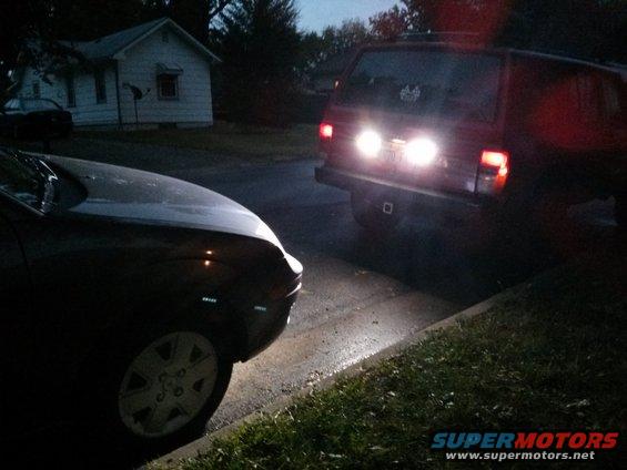 Dark SUVs parked on a street, one with brake lights on