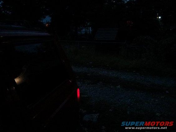 Darkness obscures most of a vehicle, only its red taillight is clearly visible