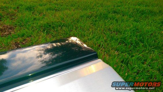 Close-up of a vehicle's tailgate with a dark green top section and silver lower section, resting on grass