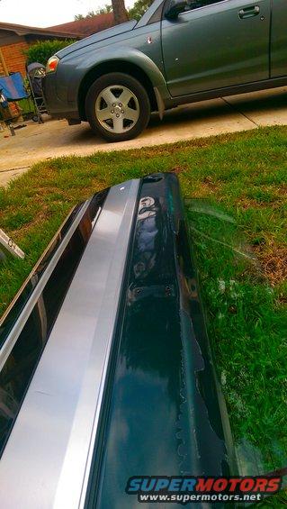 Dark green car bumper with silver stripe, peeling paint on the right side