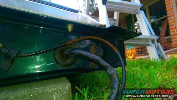 Close-up of a green vehicle part with black wiring and a brown wire bundle exiting a grommet