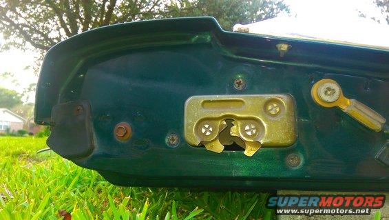 Close-up of a green tailgate's interior latch mechanism with visible screws and a yellow lever