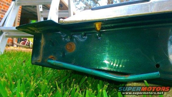 Green metallic car part with rust and a metal bar, on grass