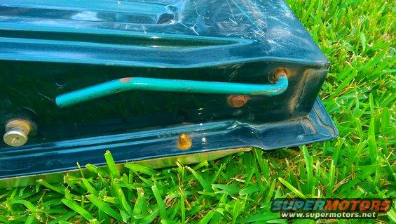 Green metal object with a teal handle and rusty bolts, resting on grass