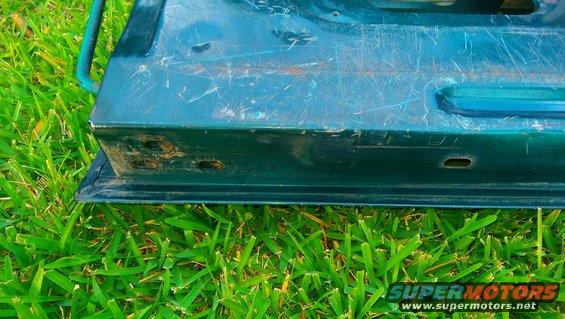 Close-up of a green vehicle door's bottom edge with grass in the background