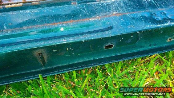 Close-up of a green vehicle door's bottom edge, showing rust and scratches
