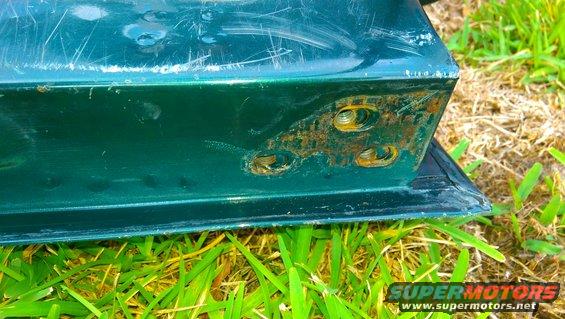 Green tailgate corner showing rust around bolt holes and scratches on the paint