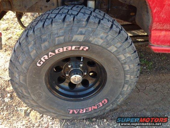 Close-up of a General Grabber off-road tire on a black wheel, part of a red vehicle visible