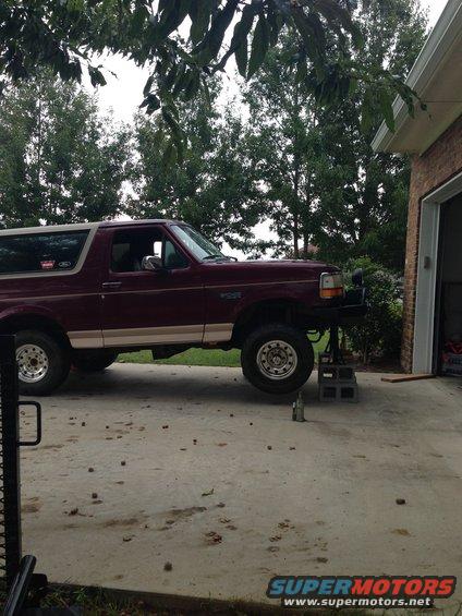Maroon Ford Bronco on jack stands in front of a garage