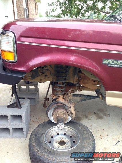 Maroon Ford Bronco with front wheel removed, supported by jack stands and cinder blocks