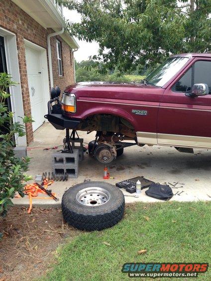 Maroon 1996 Ford Bronco front end raised for lift kit install, wheel removed
