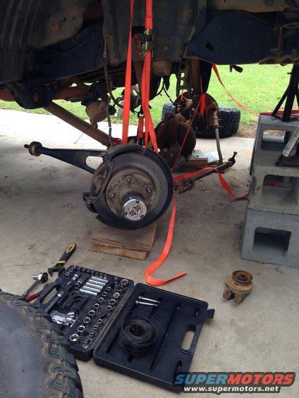 vehicle's front suspension disassembled, held up by straps, with tools on the ground