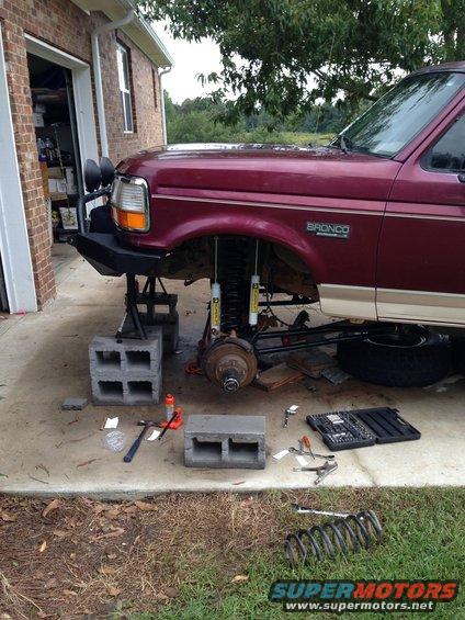 Red 1996 Ford Bronco front suspension removed, jacked up with cinder blocks