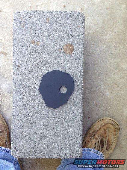 Black metal part with a hole on a cinder block, with feet visible on either side