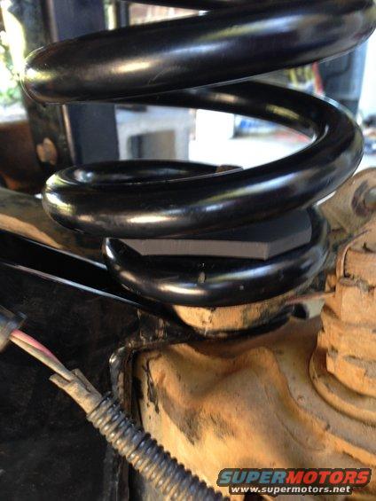 Close-up of a black coil spring on a vehicle's suspension with a black spacer block
