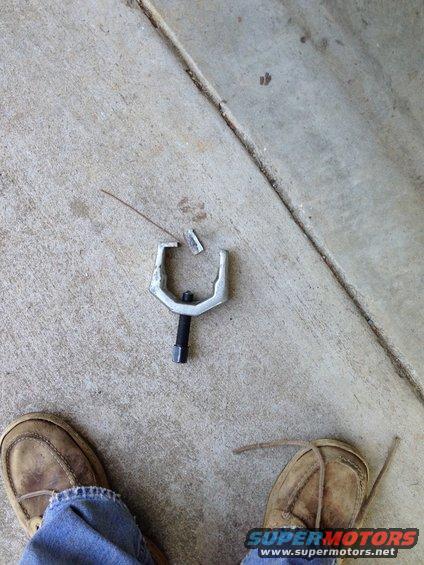 Ball joint separator tool on concrete with two pairs of feet and jeans visible