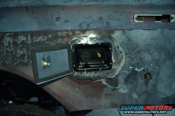Fuel filler door open showing cap and brass fitting on a vehicle body