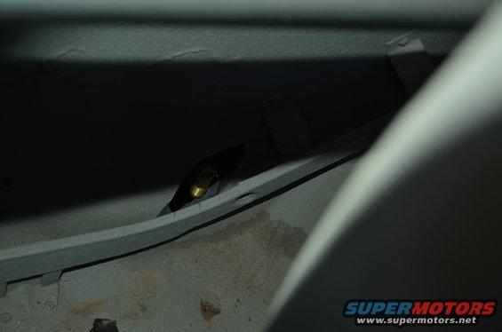 Close-up of a metal bracket with a brass fitting inside a dark vehicle interior