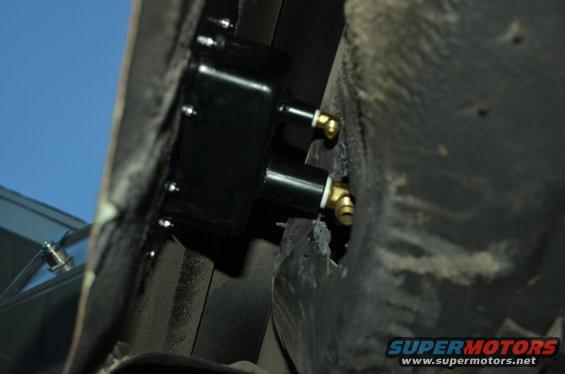 Black component with brass fittings attached to the underside of a vehicle